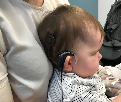Peuter met een cochleair implantaat tegen de schouder van een volwassene